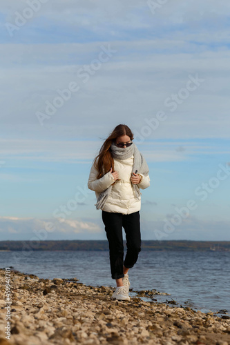 Fototapeta Naklejka Na Ścianę i Meble -  a girl in a light jacket and with a gray scarf on the bank of the Volga