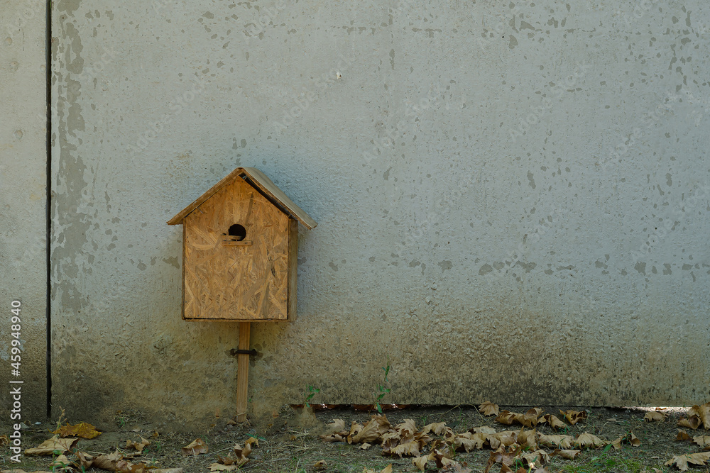 Unusually mounted birdhouse. A wooden birdhouse stands at the bottom of a concrete fence. Selective focus.