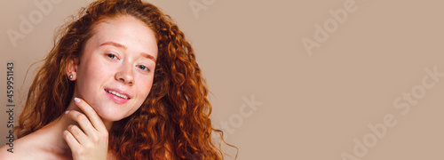 close-up portrait of a beautiful smiling girl with long curly red hair looks on a beige background. No makeup, no retouching, copy space photo