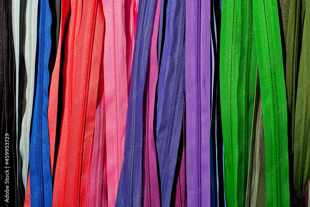 Multicolored zipper locks in a clothing store. Many colored strips of fabric hang on the wall. Clothing accessory close up.