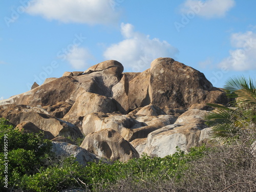 Beige and brown boulders against a blue sky with clouds. Rocks and green vegetation. Stoney bay, Virgin Gorda, British Virgin Islands, Caribbean