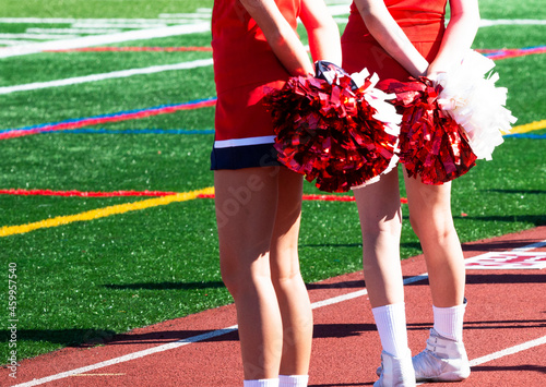 Two cheerleaders holding their red and white pom poms bshind their back