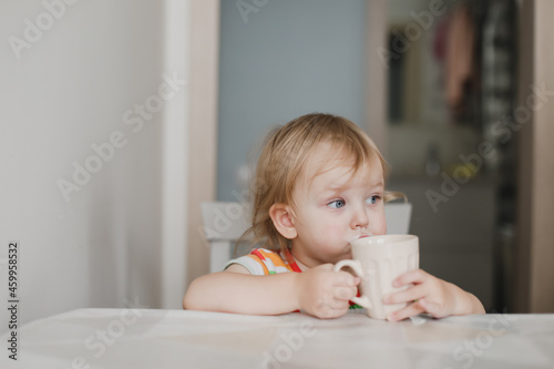 funny little girl drinking milk sitting in the kitchen