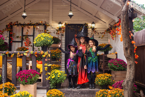 Happy Halloween! Three cute little laughing girls in witches costumes are coming to the house for sweets. © Ksenia Belyaeva