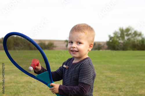 Little boy during tennis training or workout. Preschooler playing badminton in summer park. Child with small tennis racket and ball. Kid tennis player photo