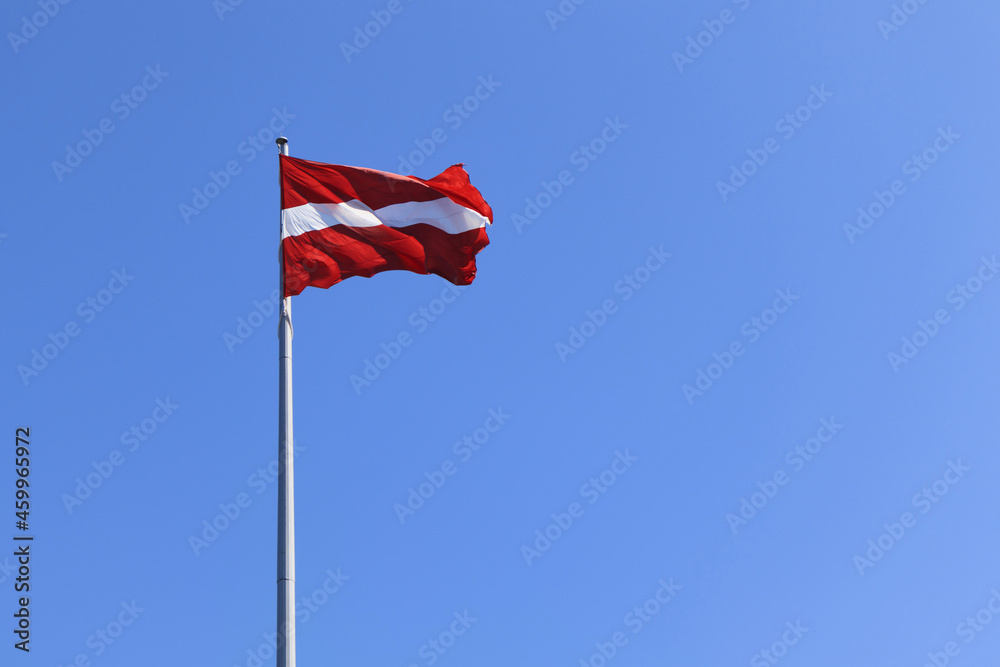 Latvian national flag on a background of blue sky