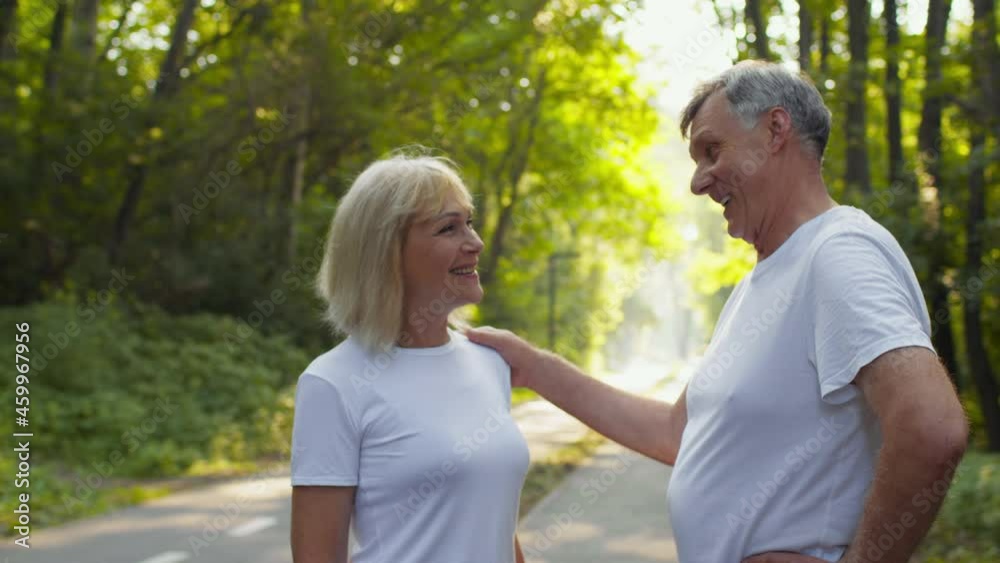 Positive retirement concept. Cheerful senior man and lady talking to each other, standing in public park and laughing