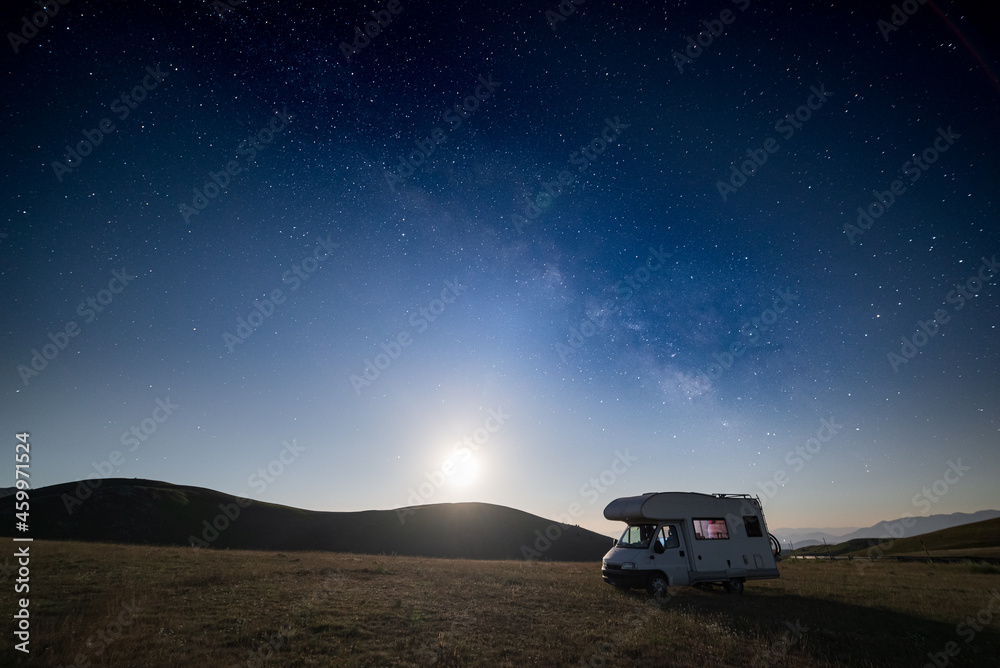 Night sky over Campo Imperatore highlands, Abruzzo, Italy. The Milky Way galaxy and stars by moon light over illuminated camper van.