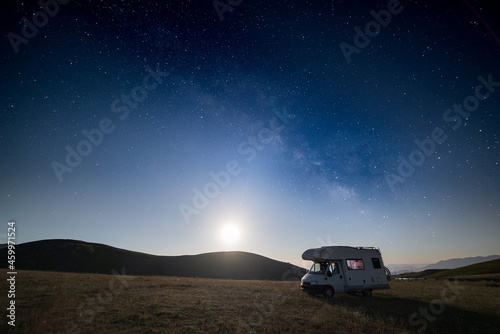 Night sky over Campo Imperatore highlands, Abruzzo, Italy. The Milky Way galaxy and stars by moon light over illuminated camper van.