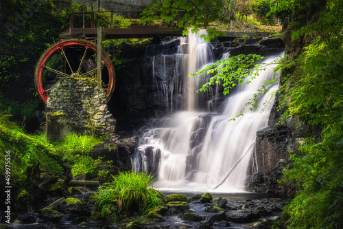 Stream leading to red waterwheel and waterfall in Glenariff Forest Park  County Antrim  Northern Ireland. Long exposure and soft focus photography