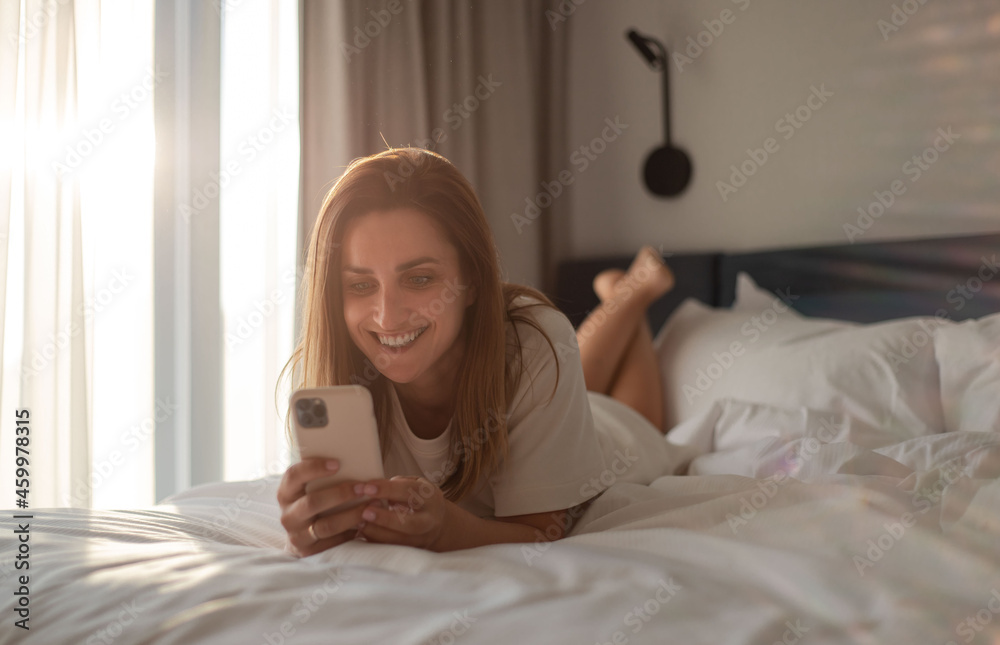 Happy woman lying on bed and using smartphone in bedroom. Happy woman lying on bed and using smartphone in bedroom.