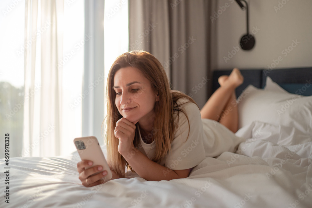 Happy woman lying on bed and using smartphone in bedroom. Happy woman lying on bed and using smartphone in bedroom.
