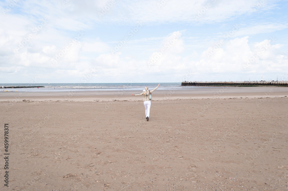 tiny woman runs open arms along the beach to the sea