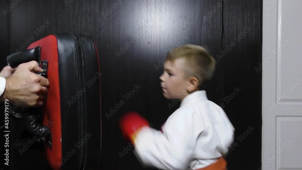 Boy athlete with red pads on his hands trains punches on the simulator Boy athlete with red pads on his hands trains punches on the simulator