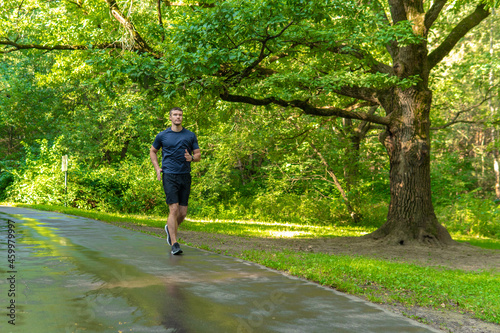 A man athlete runs in the park outdoors, around the forest, oak trees green grass young enduring athletic athlete active runner forest, fitness trail young legs motion, woods outside. Summer energy
