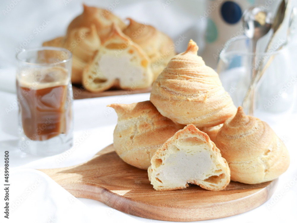 French choux dough pastry cream puff, filled with white sweet cream with a cup of coffee on table French choux dough pastry cream puff, filled with white sweet cream with a cup of coffee on table