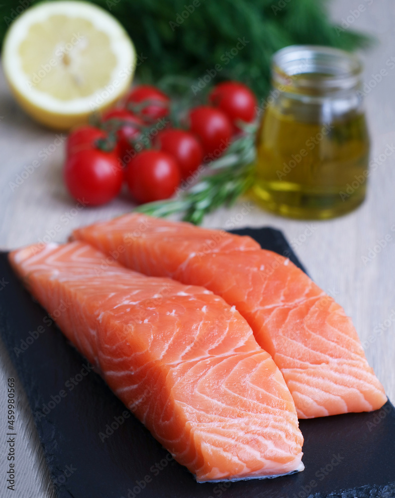Fillet of fresh raw salmon with vegetables and ingredients with a bottle of olive oil, it's a common food fish classified as an oily fish with a rich content of protein and omega-3 fatty acids Fillet of fresh raw salmon with vegetables and ingredients with a bottle of olive oil, it's a common food fish classified as an oily fish with a rich content of protein and omega-3 fatty acids