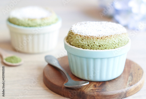 A fluffy Matcha green tea soufflé a French dessert on a wooden plate with icing sugar powder on top with spoon. A soufflé is a baked egg-based dish which originated in early eighteenth century France 