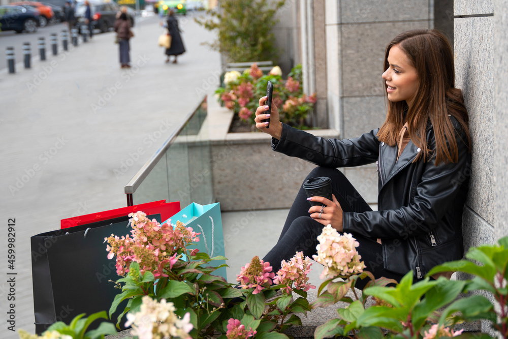Fototapeta premium Pretty young woman drinking coffee and doing selfie after the shopping in a mall. Happy lifestyle, holiday discounts and sales concept.