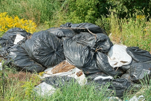 black and white plastic garbage bags in a heap in green grass in nature