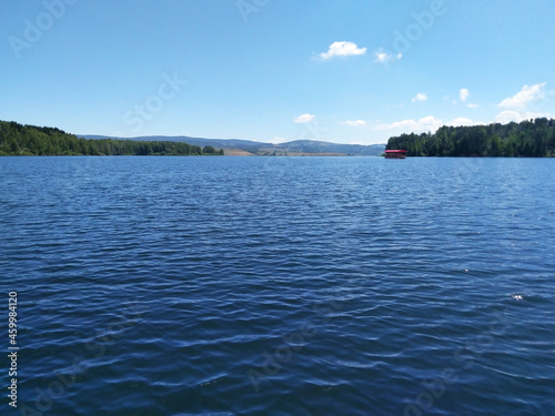View of a beautiful mountain lake. In the background is a tourist boat  forest  hills and blue sky. Vlasina lake  Serbia