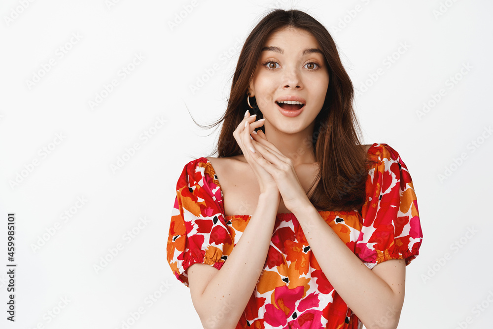 Image of beautiful girl looking excited in awe, gazing with amazement and anticipation, standing in floral dress over white background Image of beautiful girl looking excited in awe, gazing with amazement and anticipation, standing in floral dress over white background