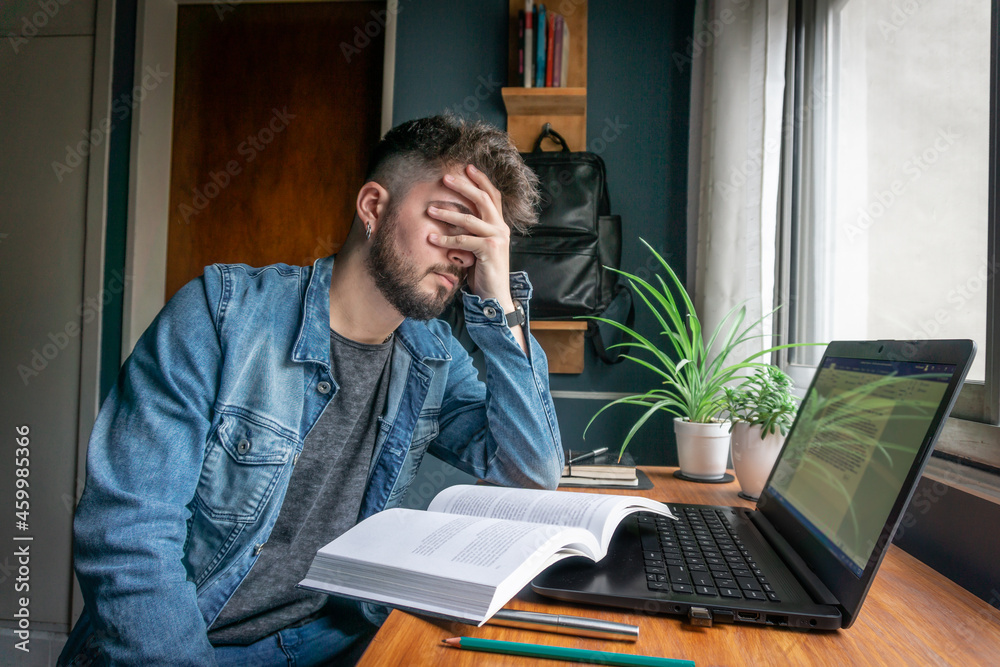 young college student tired of studying from a book and laptop young college student tired of studying from a book and laptop