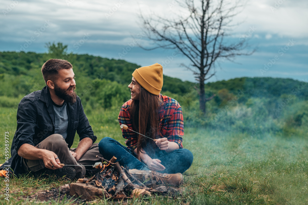 Couple of campers sitting next to the camping fire and eating marshmallows Couple of campers sitting next to the camping fire and eating marshmallows