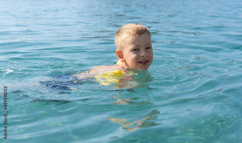 The child learns to swim. Happy child swims in the sea. Holidays in Greece The child learns to swim. Happy child swims in the sea. Holidays in Greece