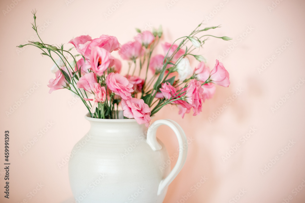 Bouquet with eustoma, summer flowers in a white vase, on a pink-beige background.
