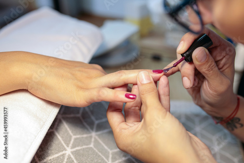 Close-up view of unrecognizable female manicurist carefully applying red gel nail polish