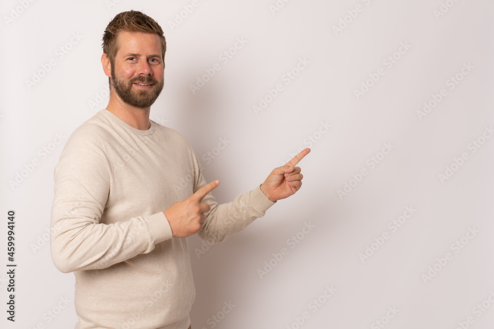 Young man with sweater pointing to the side with a finger to present a product or an idea while looking forward smiling on isolated white background Young man with sweater pointing to the side with a finger to present a product or an idea while looking forward smiling on isolated white background