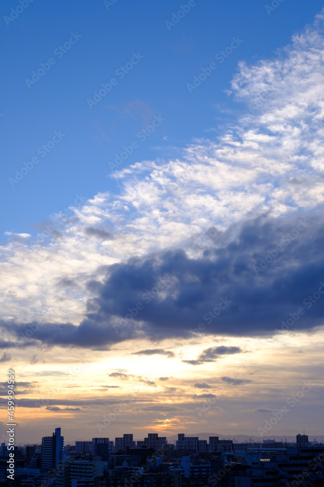都会の夕暮れ。六甲山に沈む夕陽とオレンジ色に染まる雲と空。