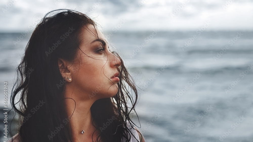 portrait of brunette woman in profile looks to right with wet flying hair against background of sea portrait of brunette woman in profile looks to right with wet flying hair against background of sea