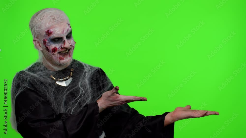 Creepy man with bloody scars face, Halloween stylish zombie make-up. Scary wounded undead guy showing thumbs up and pointing at right on blank space. Place for advertisement logo. Sinister monster Creepy man with bloody scars face, Halloween stylish zombie make-up. Scary wounded undead guy showing thumbs up and pointing at right on blank space. Place for advertisement logo. Sinister monster