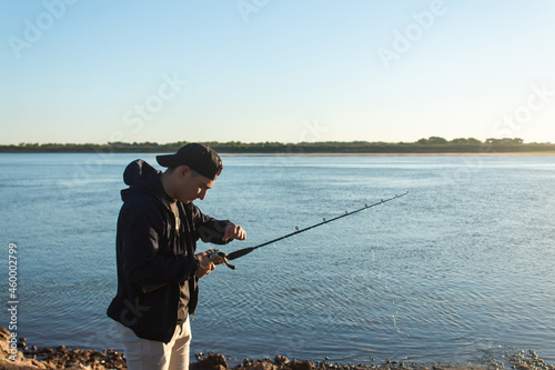 Young man preparing his fishing rod at the edge of the river.