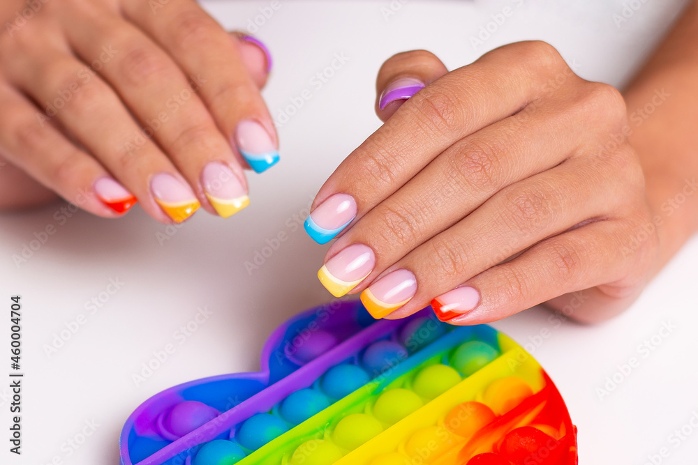 Beautiful female hands with colourful manicure nails holding toy, pop it Beautiful female hands with colourful manicure nails holding toy, pop it
