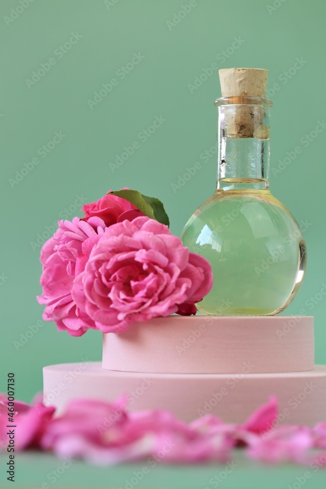 Essential rose oil. Aromatherapy and massage.Rose oil and pink roses on a pink podium on light green background.Rose essential oil. Organic bio cosmetics. 