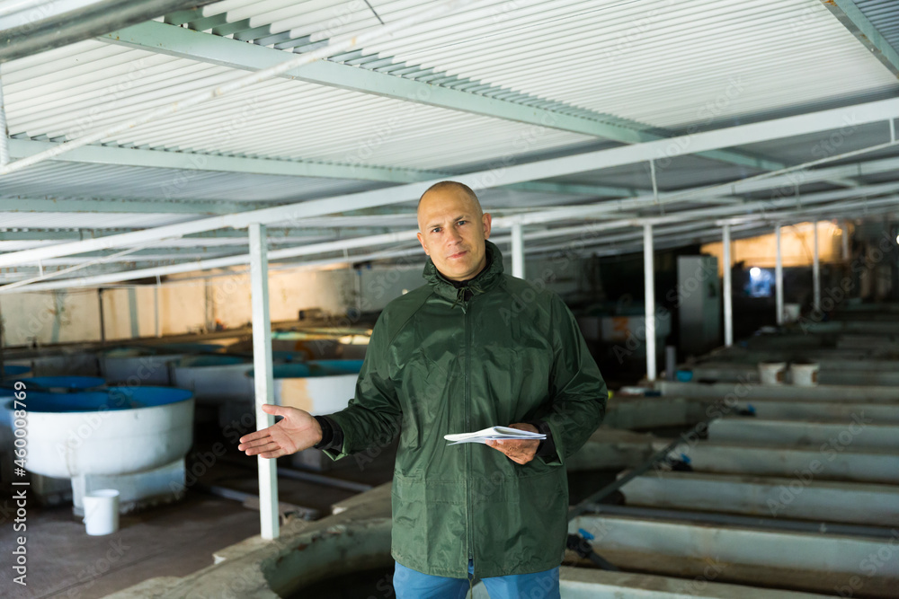 Confident farmer engaged in industrial breeding of trout, demonstrating fry rearing tanks on his farm..