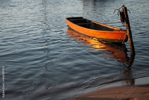 Small orange wooden boat moored to a pole at the edge of the lake during sunset. Small boat for fishermen. © Horacio Selva