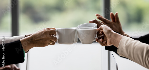 Closeup shot of cups of coffee in hands of unrecognizable unidentified businesswoman colleague group in formal business clothing cheering toasting celebrating together after finish planning working photo