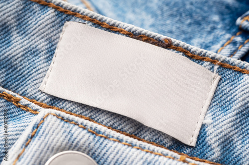 Blue jeans with a white blank label, close-up. Jeans texture. Fashion denim background for sewing, copy space. Label on clothing to indicate the size, company