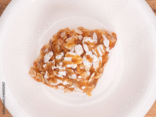 top angle of fresh croissant covered almond slide mixed sweet caramel and topping with sugar powder on a white plate placed on white table top.