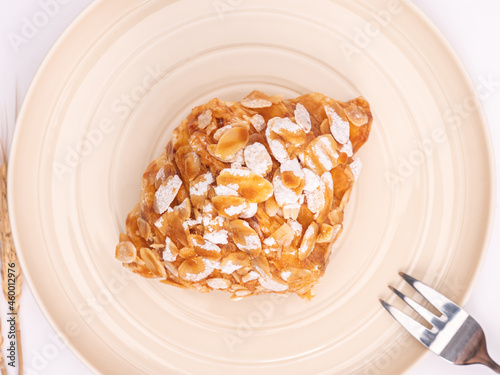 top angle of fresh croissant covered almond slide mixed sweet caramel and topping with sugar powder on a pastel plate placed on white table top.