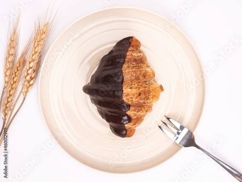 top angle of fresh croissant covered chocolate and topping with chocolate powder on a pastel plate placed on white table top. food concept on photography image.