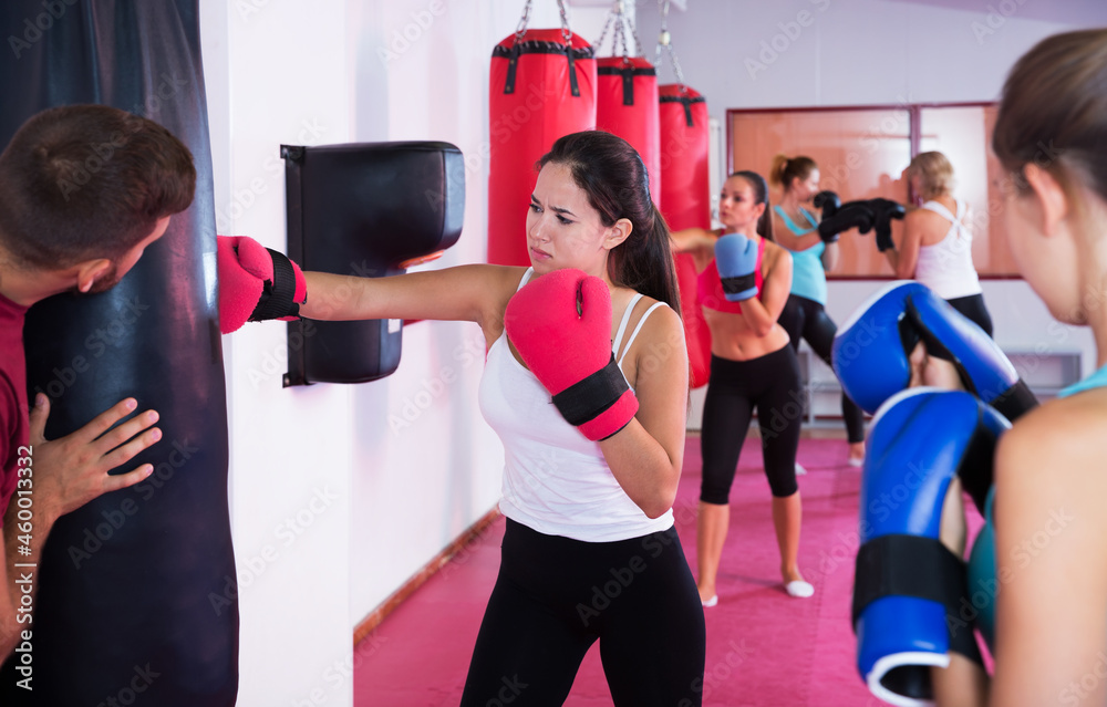 Portrait of sporty female boxer who is training with punching bag in fitness club