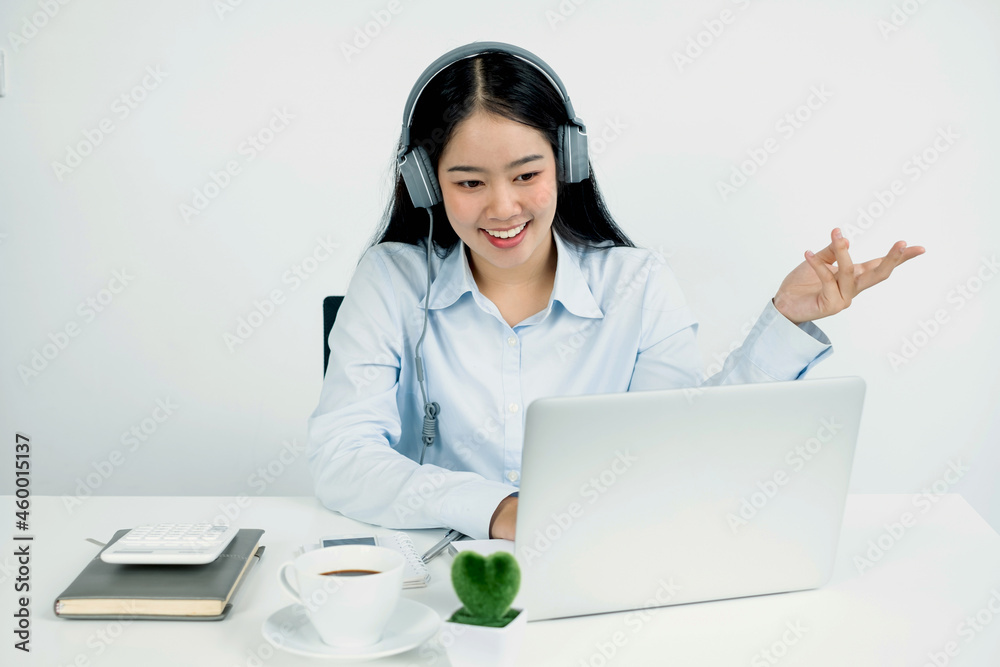 Video call, a young Asian woman wearing headphones, communicates via online video long distance, looking at the digital laptop screen, happily greeted with a friend Video call, a young Asian woman wearing headphones, communicates via online video long distance, looking at the digital laptop screen, happily greeted with a friend