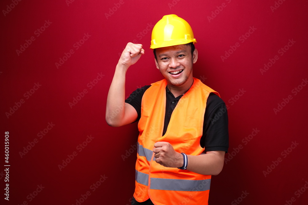 Happy excited and smiling young Asian man worker raising his arm up to celebrate success or achievement.