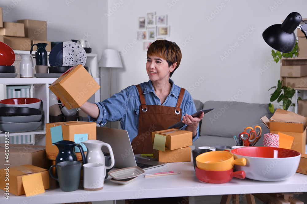 Mature Asian woman entrepreneur, Business owner checking address and delivery detail before shipping product. Online selling business work at home concept Mature Asian woman entrepreneur, Business owner checking address and delivery detail before shipping product. Online selling business work at home concept