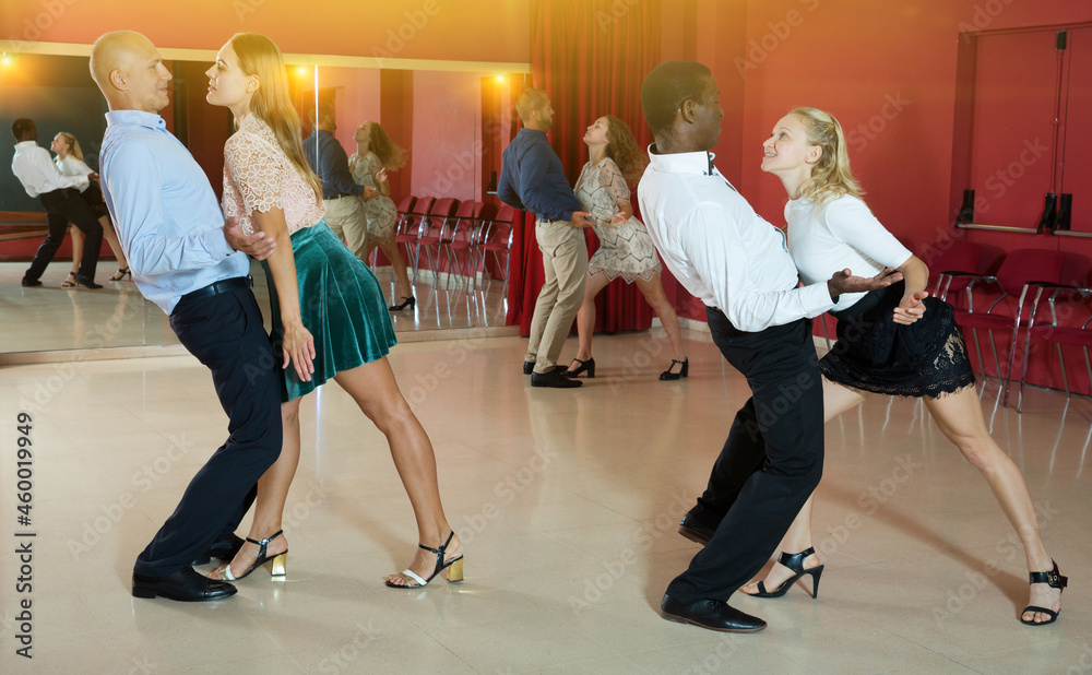 Fototapeta premium Smiling adult pairs dancing tango movements in modern dance studio